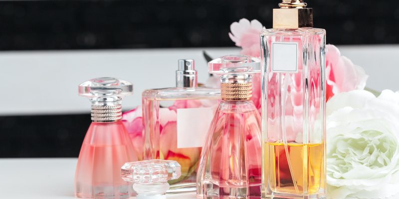 Bottles of perfume with flowers on light background